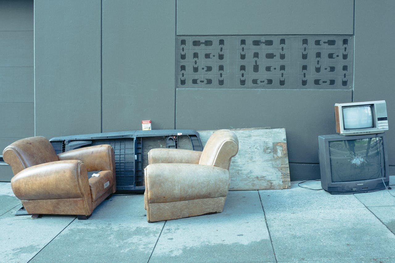 Sidewalk scene with vintage chairs and old televisions against a wall.